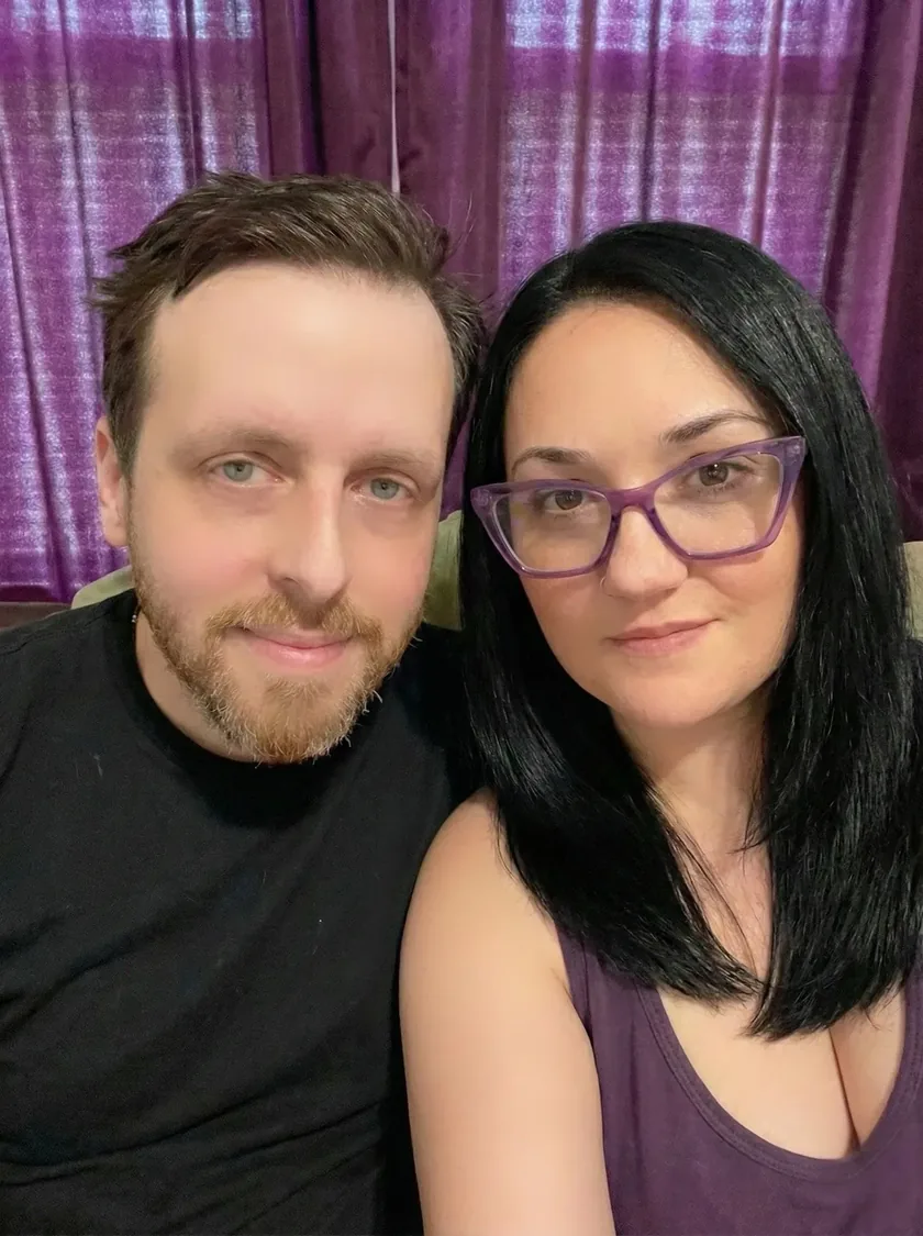 Ty, founder of Cloudwerx Laboratories, and his wife Sizzlebop, sitting side by side in front of a purple curtain.